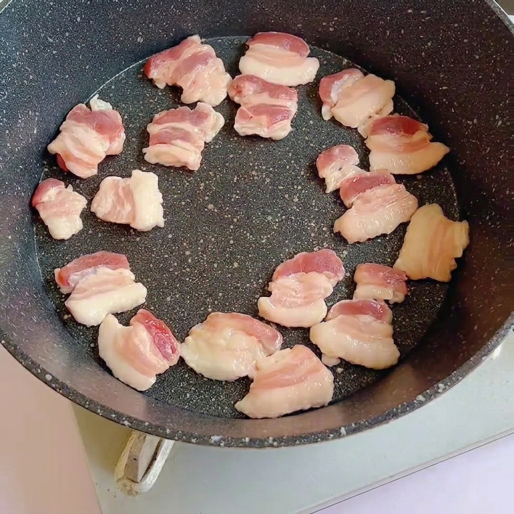 Rodajas de panceta cruda en una sartén caliente empezando a dorarse.