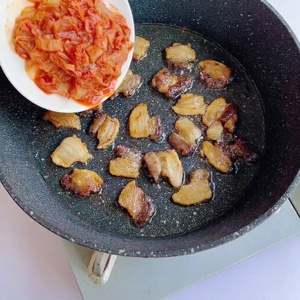 Kimchi picado siendo añadido a la sartén con la panceta dorada.