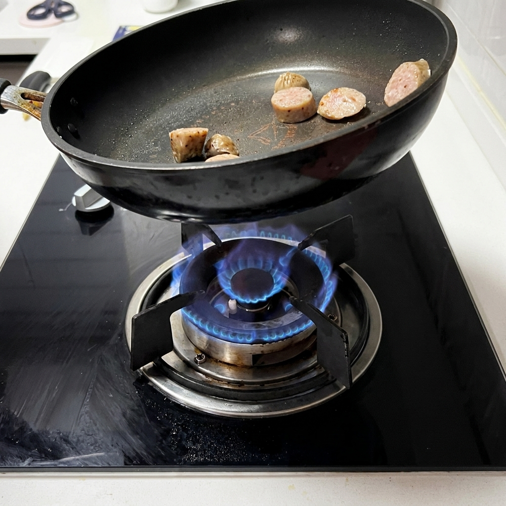 Rodajas de salchicha sofriéndose y dorándose en una sartén negra sobre una estufa de gas.