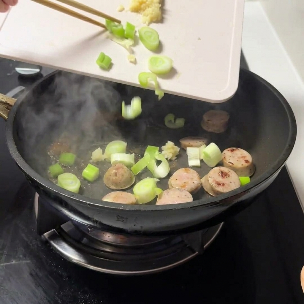 Cebollino picado y ajo picado siendo añadidos a la sartén con la carne.