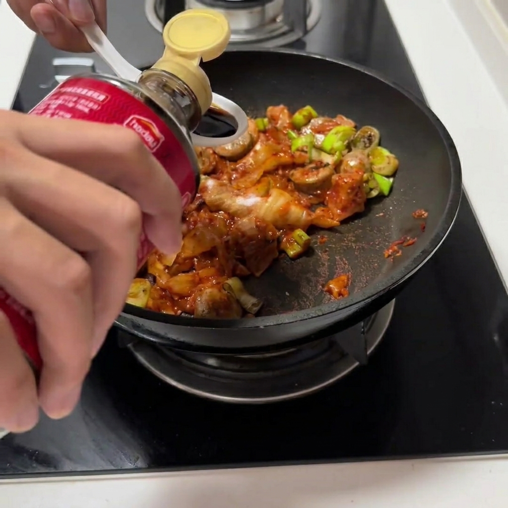 Salsa de soja y salsa de ostras siendo vertidas en la sartén con la mezcla de kimchi.