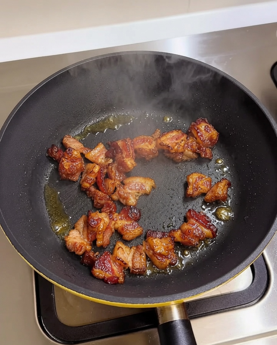 Trozos de panceta de cerdo dorándose en una sartén caliente.