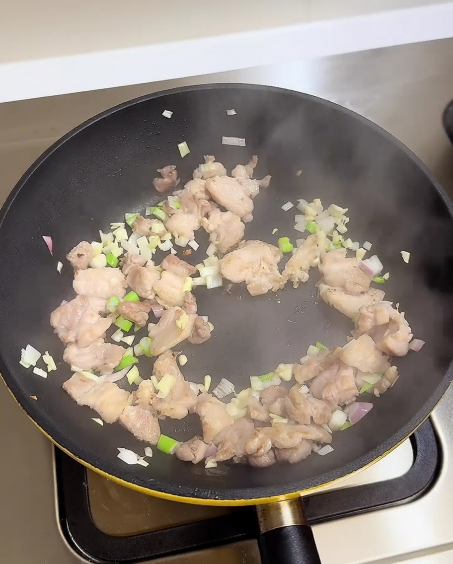 Panceta de cerdo, cebolletas, ajo y cebolla salteándose en una sartén con líquidos sazonadores.