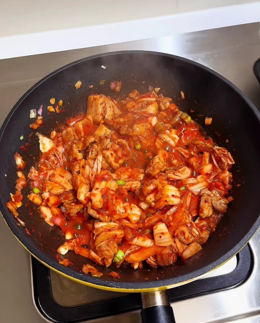 Arroz blanco cocido añadiéndose a una sartén que contiene kimchi y panceta de cerdo salteados.