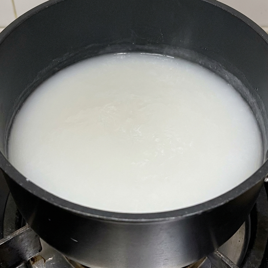 Una pasta espesa de harina de arroz glutinoso cocinándose en una olla negra.