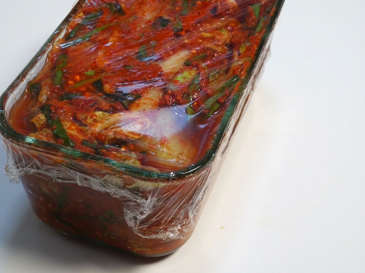 Recipiente de kimchi fermentado con el papel film siendo retirado.