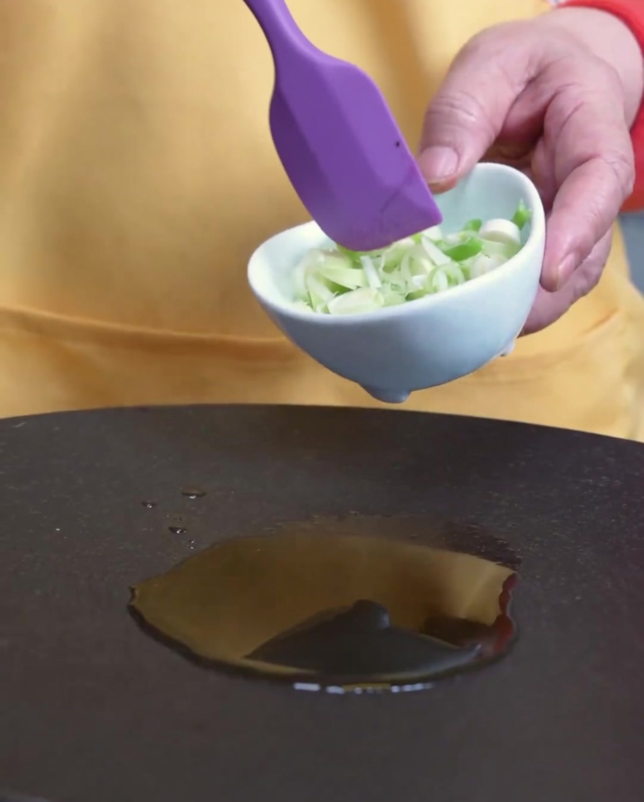 Cebolletas siendo removidas en una sartén con aceite de sésamo.