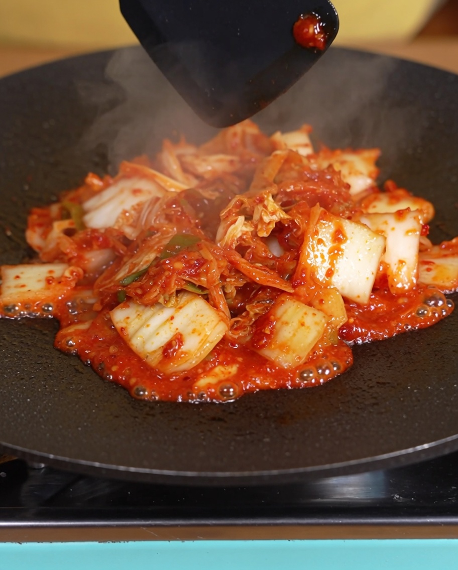 Kimchi cocinándose en la sartén con el líquido visiblemente reducido.