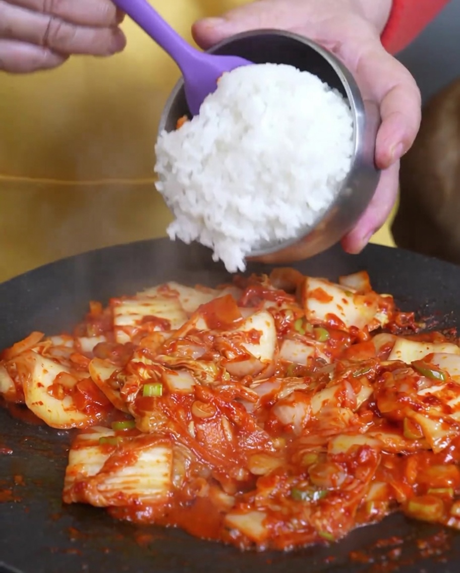Arroz blanco cocido siendo añadido a la sartén que contiene el kimchi sofrito.