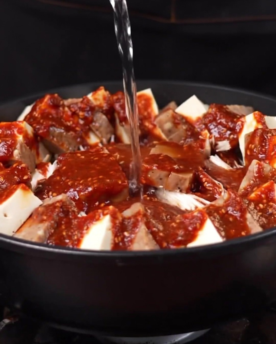 Agua hirviendo siendo vertida en la olla, combinándose con la salsa y los ingredientes.
