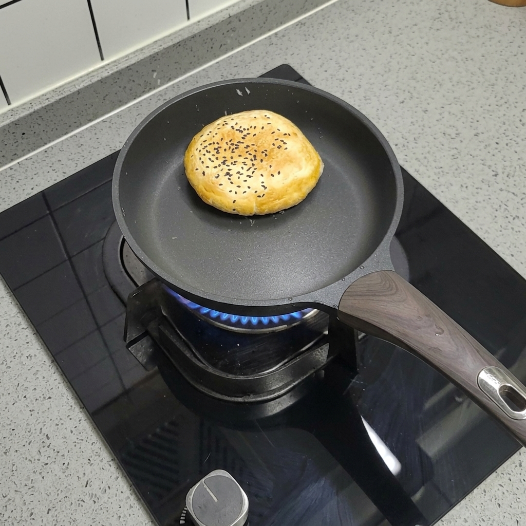 Pan de hamburguesa congelado con semillas de sésamo cocinándose en una sartén antiadherente seca.
