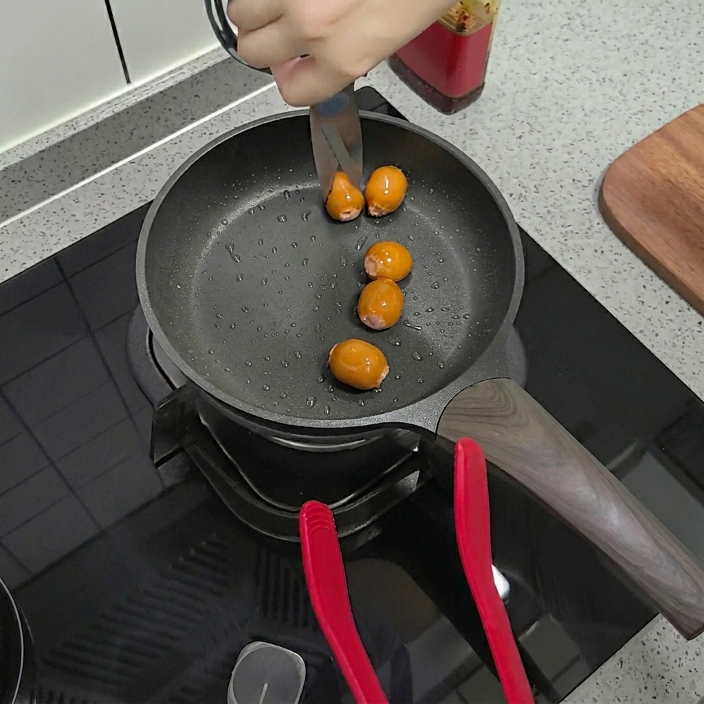 Tijeras de cocina cortando salchichas doradas directamente en la sartén.