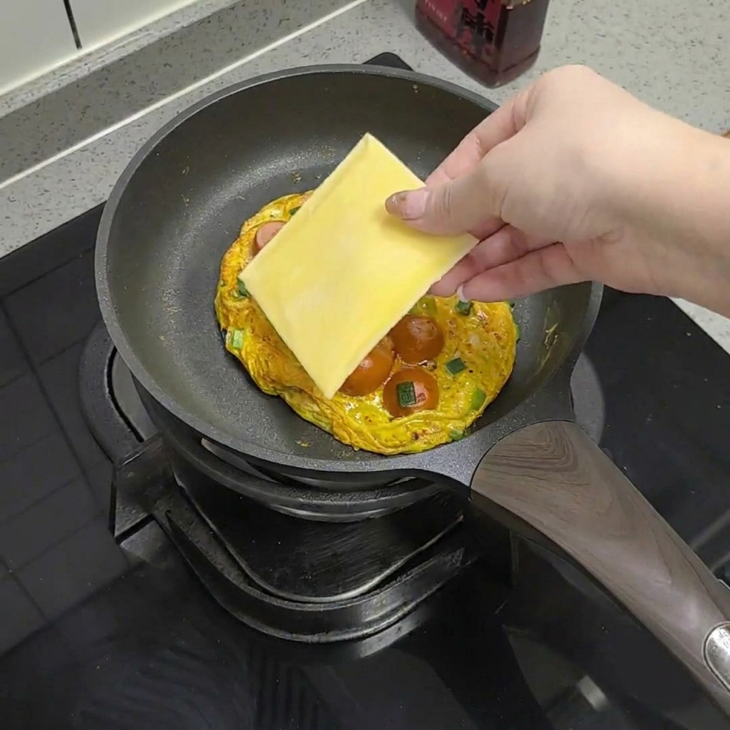 Una loncha de queso colocada sobre el huevo y las salchichas en la sartén.