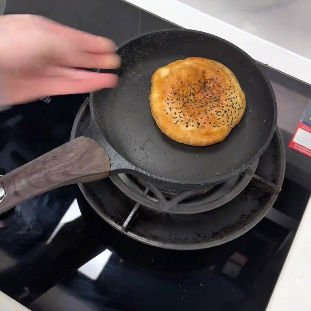 Una mano colocando un pan de sésamo negro en una sartén antiadherente.