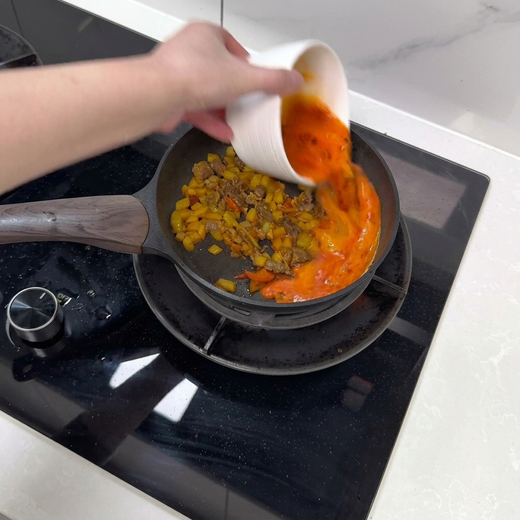 Huevo batido siendo vertido sobre la mezcla de ternera y verduras.