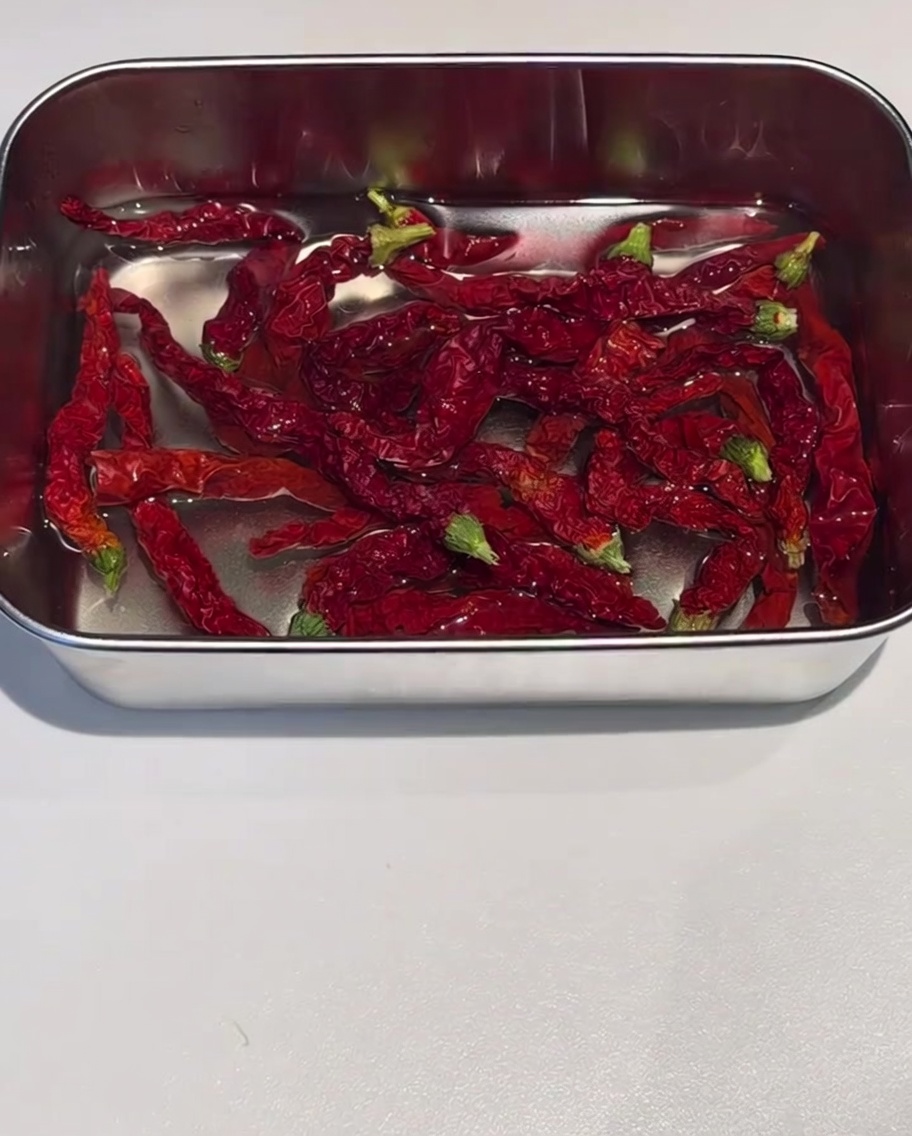 Pieles de chile rojo secas remojándose en un recipiente de acero inoxidable lleno de agua caliente.