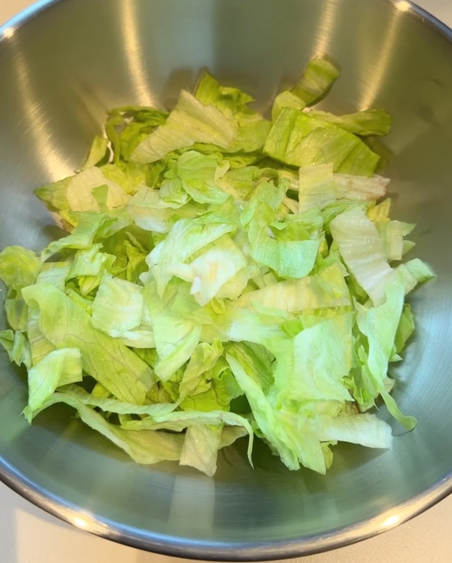 Lechuga rallada crujiente colocada en un tazón grande de mezcla de acero inoxidable.