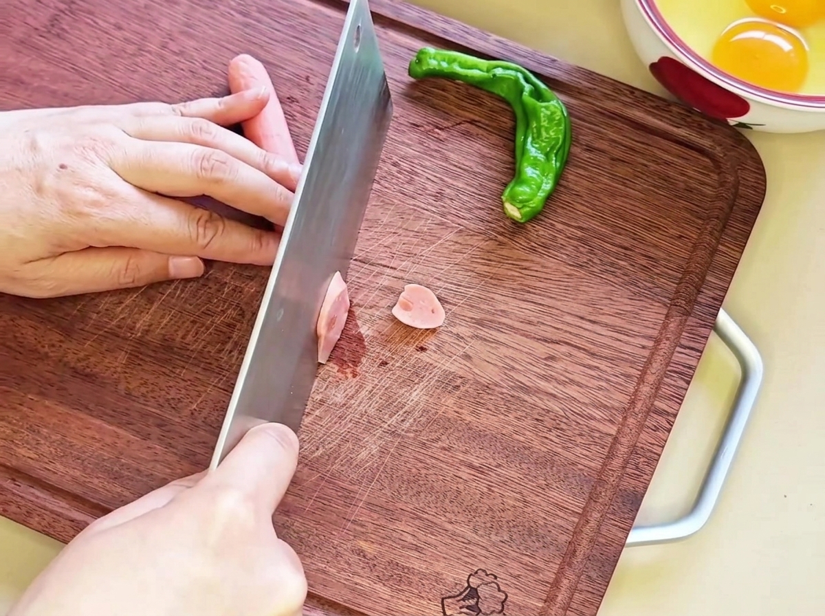 Rodajas diagonales de salchicha dispuestas ordenadamente sobre una tabla de madera, listas para el siguiente paso.