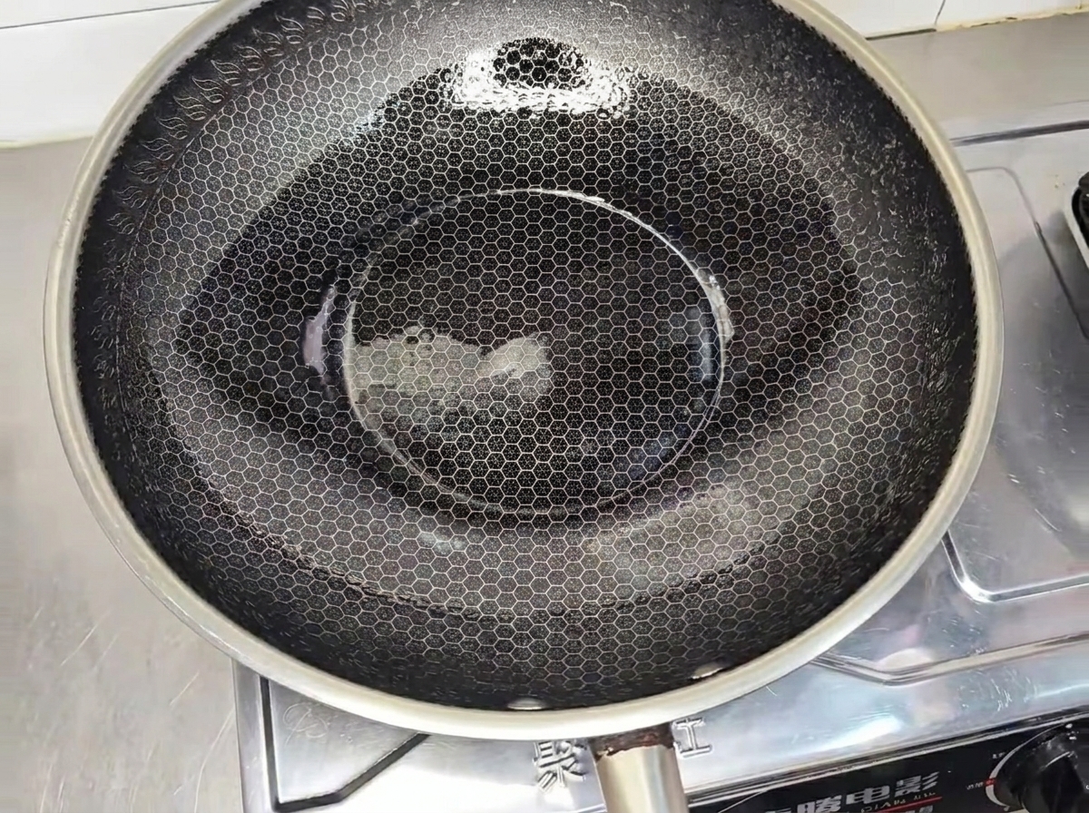 Una milanesa de pollo sazonada friéndose en un wok caliente con aceite hasta dorarse.