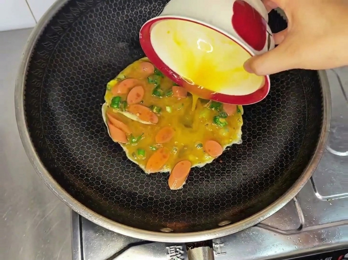 Virtiendo una mezcla de huevos crudos batidos, salchicha y chile verde desde un tazón hacia un wok caliente.