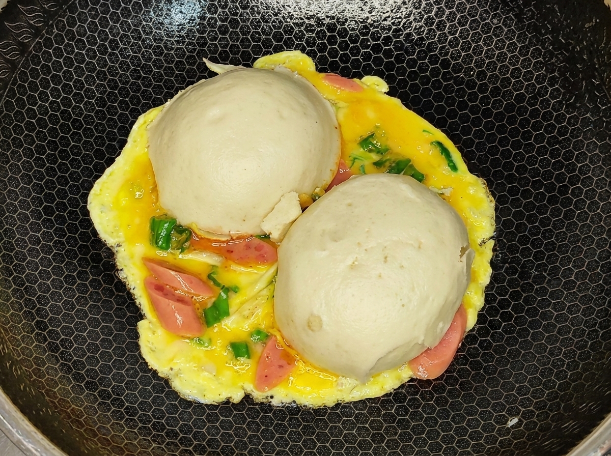 La tortilla volteada con el lado del huevo cocido hacia arriba y los panes al vapor debajo en un wok.