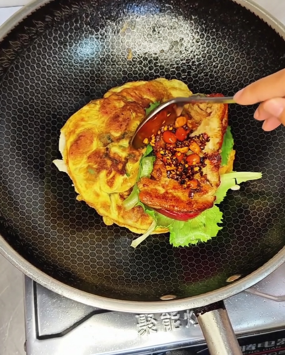 Una milanesa de pollo frita cubierta con una cucharada de salsa de chile con cacahuate colocada sobre lechuga en un wok.