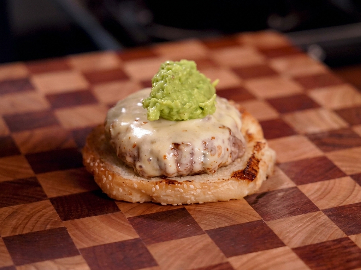 Una cucharada generosa de guacamole verde sobre una hamburguesa cubierta de queso derretido.