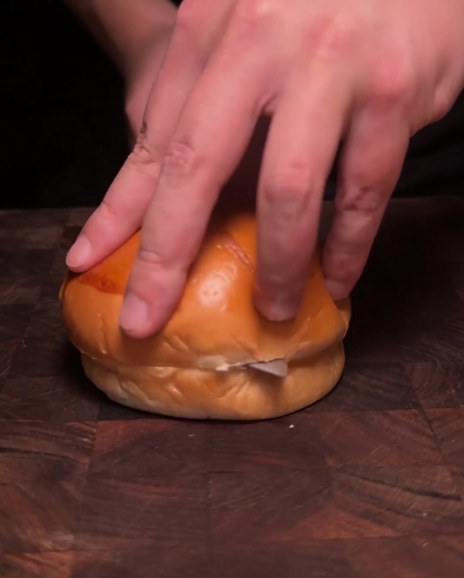 Dos mitades de pan para hamburguesa boca abajo en una sartén, tostando en mantequilla derretida hasta que estén doradas.
