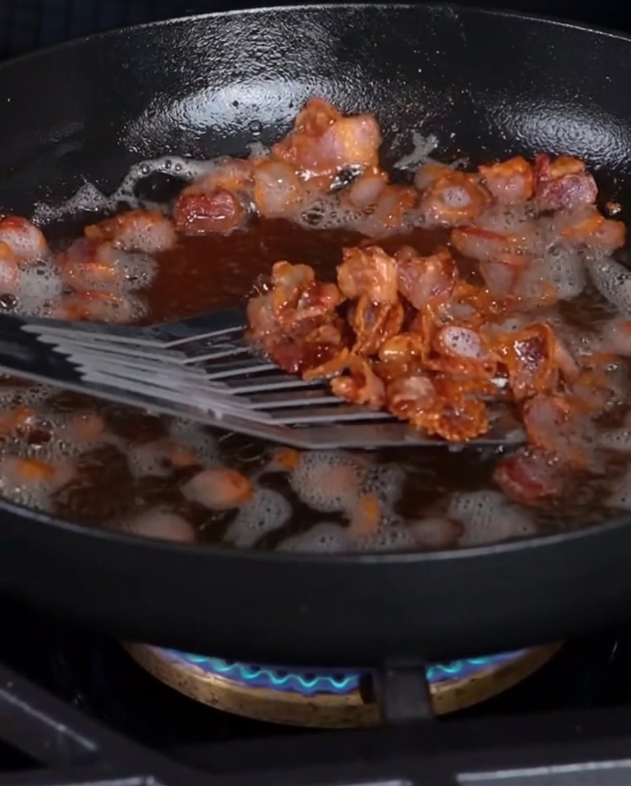 Trozos de tocino crujiente siendo retirados de la sartén con una espumadera.