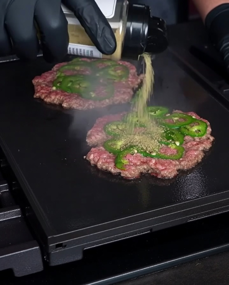Sazonando la hamburguesa aplastada sobre la plancha.