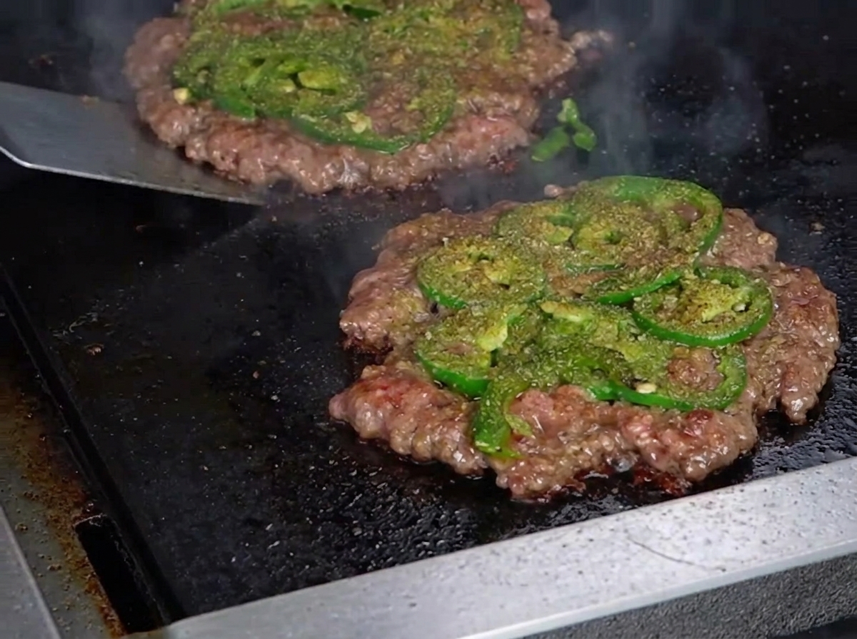 Espátula metálica volteando la hamburguesa revelando una costra dorada.