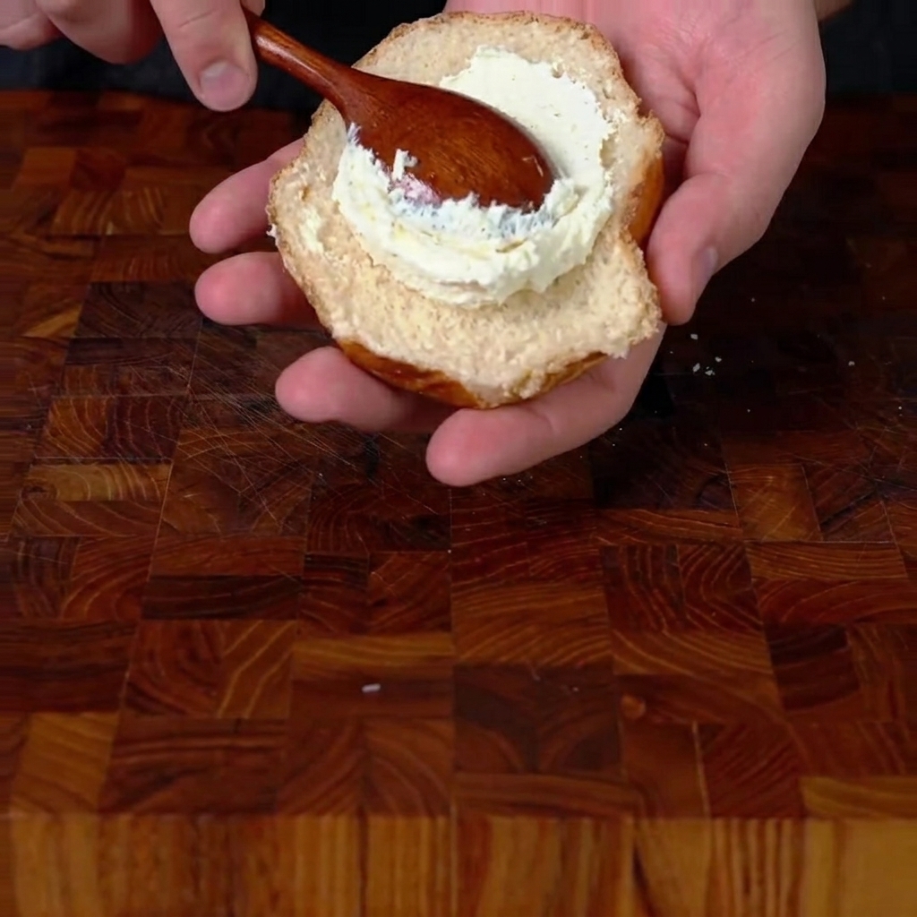 Untando queso crema sobre el pan inferior tostado.