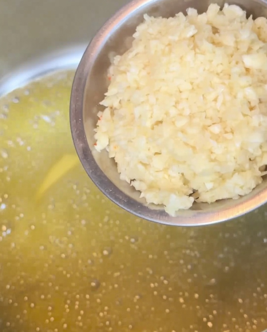 Ajo picado friéndose en una base de mantequilla derretida dentro de una olla de metal, adquiriendo un tono dorado.