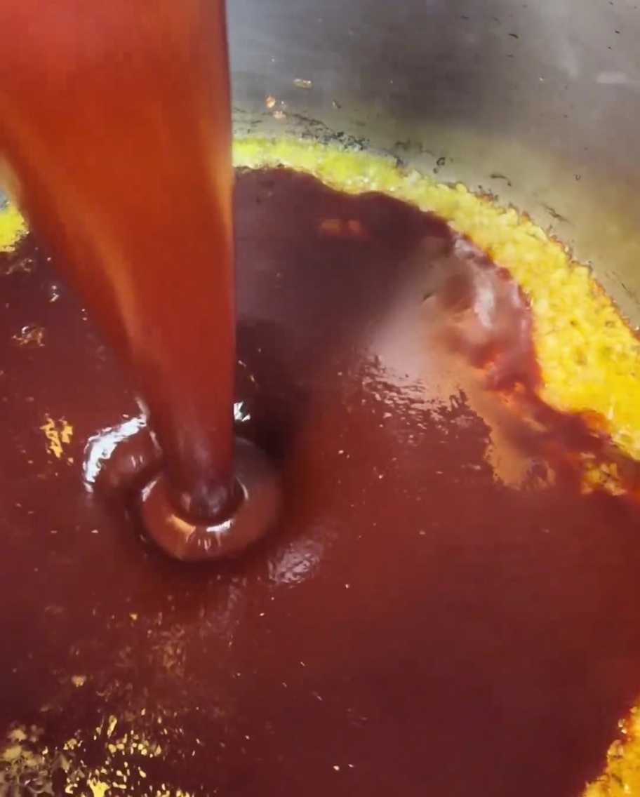 La salsa roja ya mezclada vertiéndose en una olla donde el ajo picado y la mantequilla están cocinándose a fuego lento.