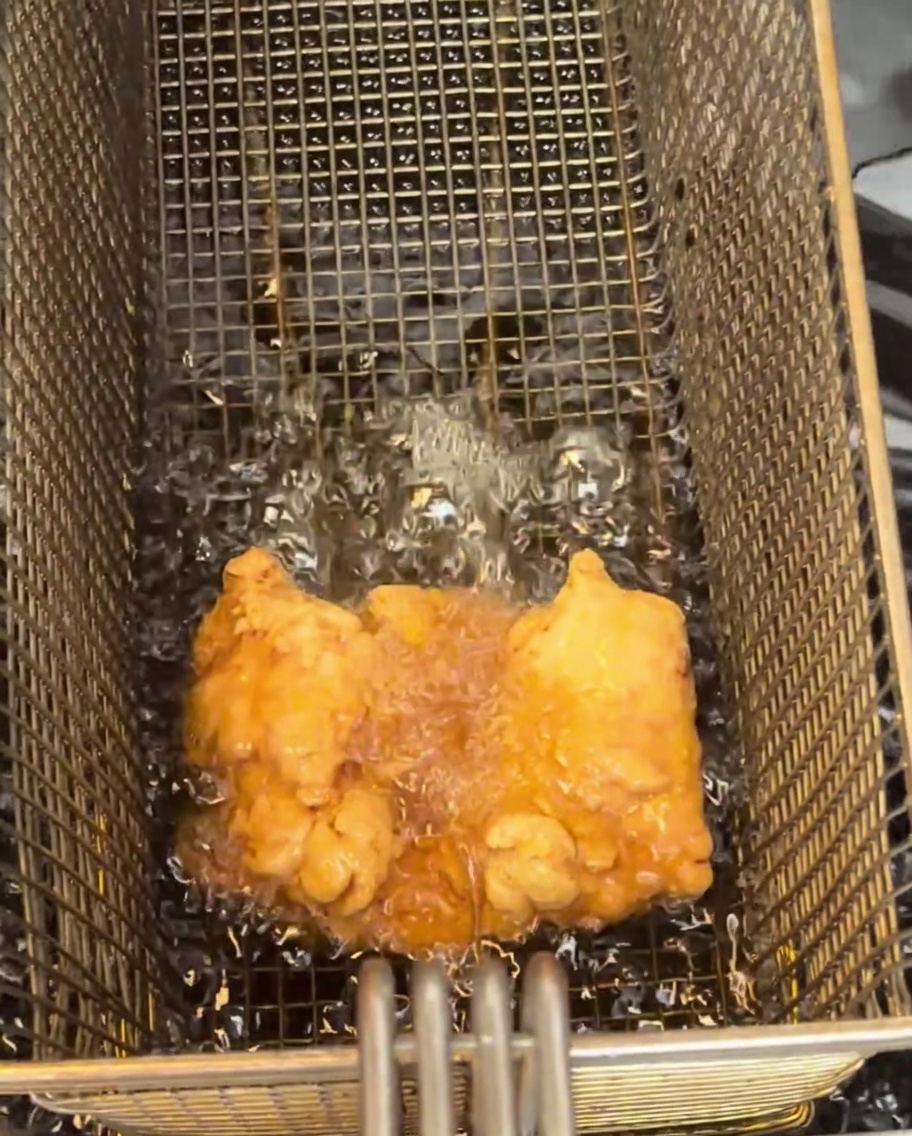 Un muslo de pollo frito, dorado y crujiente, reposando sobre una rejilla de metal para enfriar.