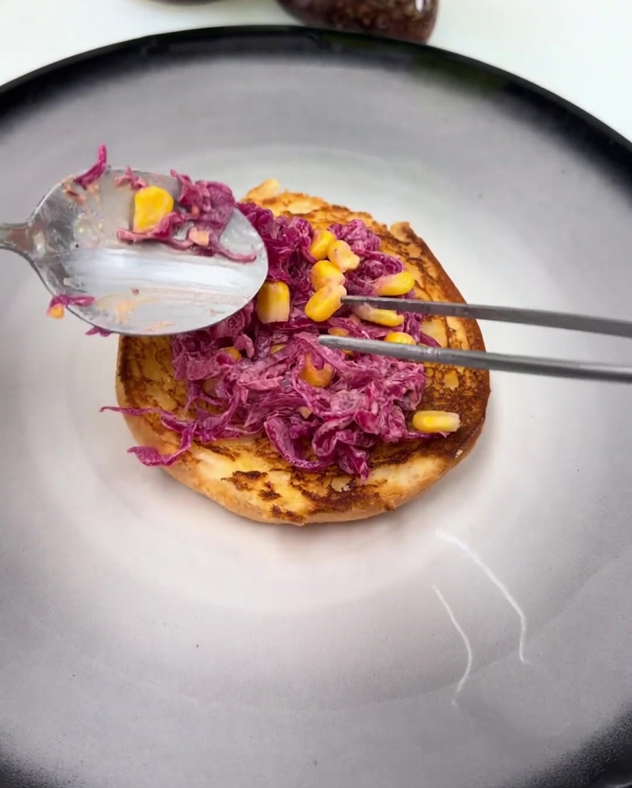 Un muslo de pollo frito brillante y cubierto de salsa descansando sobre la ensalada de col lombarda en el pan de hamburguesa.