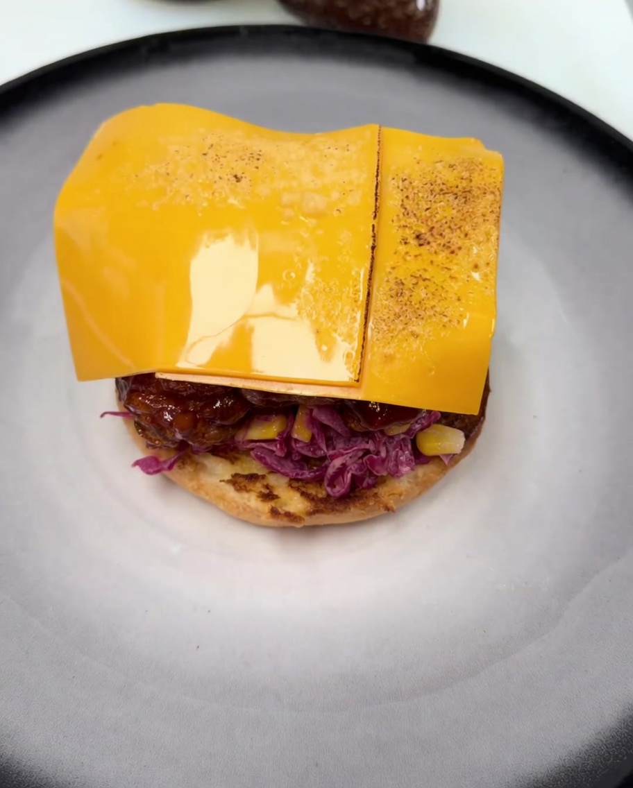 Una loncha de queso cheddar derritiéndose sobre el pollo frito glaseado, con un ligero tostado visible provocado por el soplete.