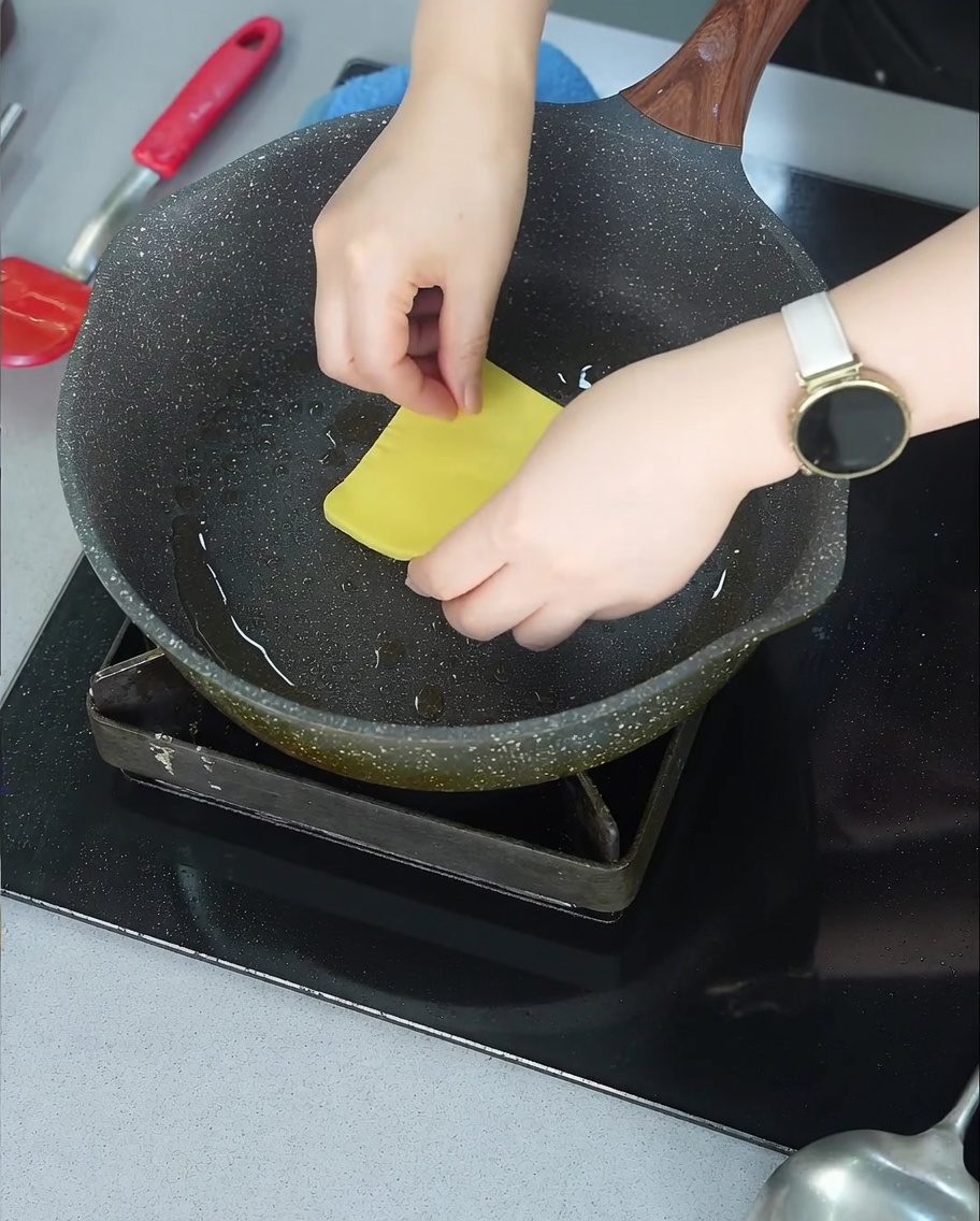 Una loncha de queso amarillo empezando a derretirse sobre una hamburguesa de ternera dorada en una sartén.