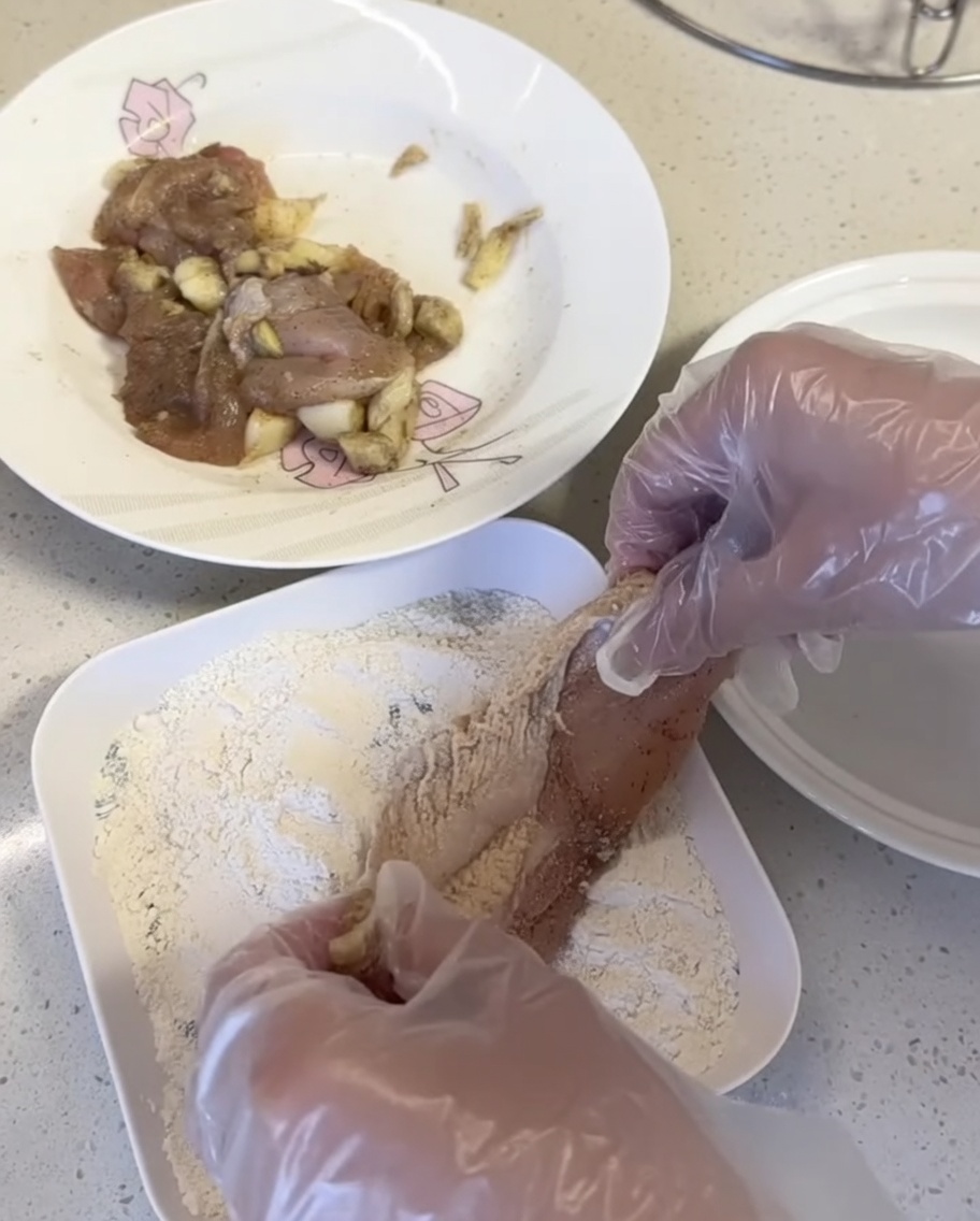 Trozos de pollo siendo presionados en mezcla para empanizar en un plato blanco.