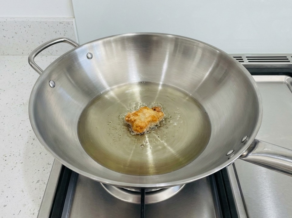 Un trozo de pollo empanizado friéndose en un wok lleno de aceite caliente.