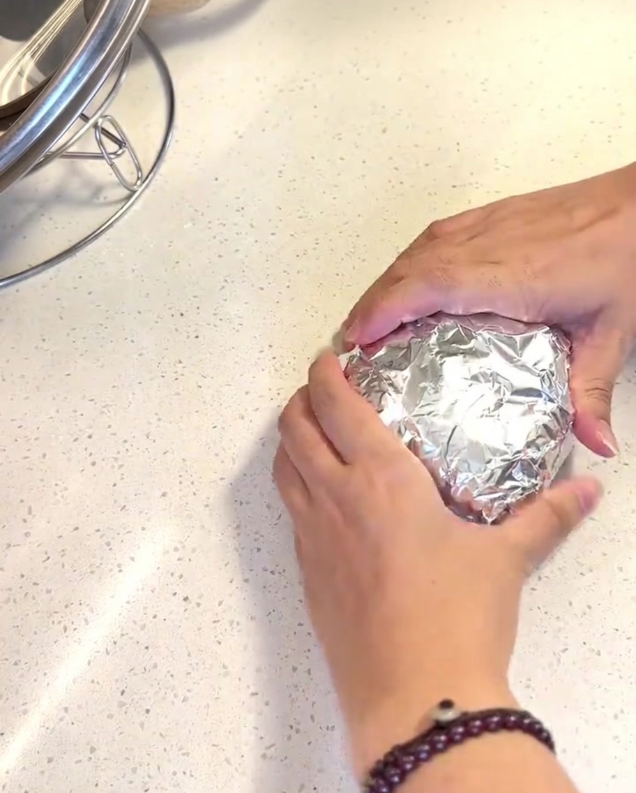 Panes de hamburguesa envueltos en papel de aluminio brillante dentro de la cesta de una freidora de aire.