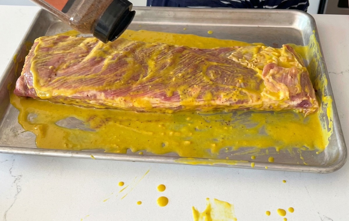 Espolvoreando sazonador seco sobre un rack de costillas cubiertas de mostaza.