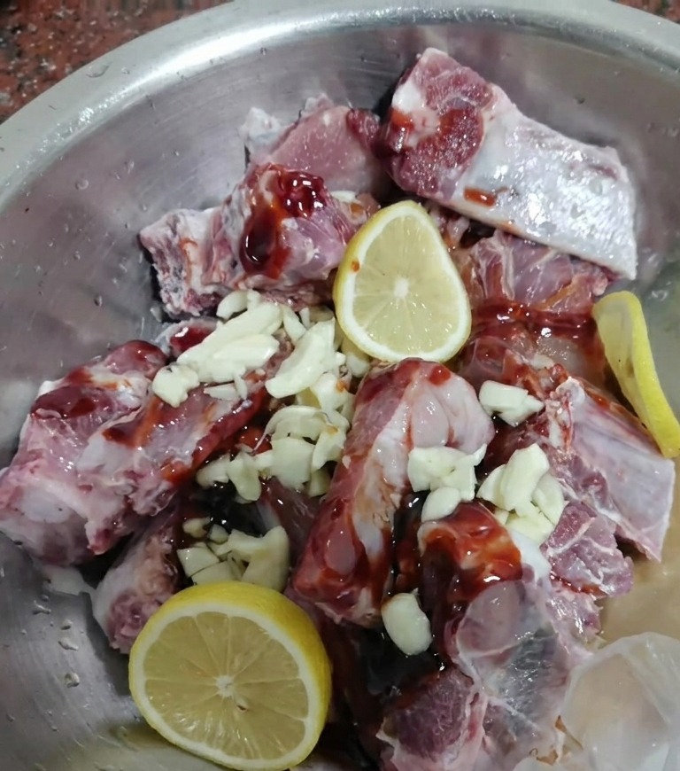 Costillas de cerdo crudas mezcladas con adobo oscuro, ajo y rodajas de limón fresco.