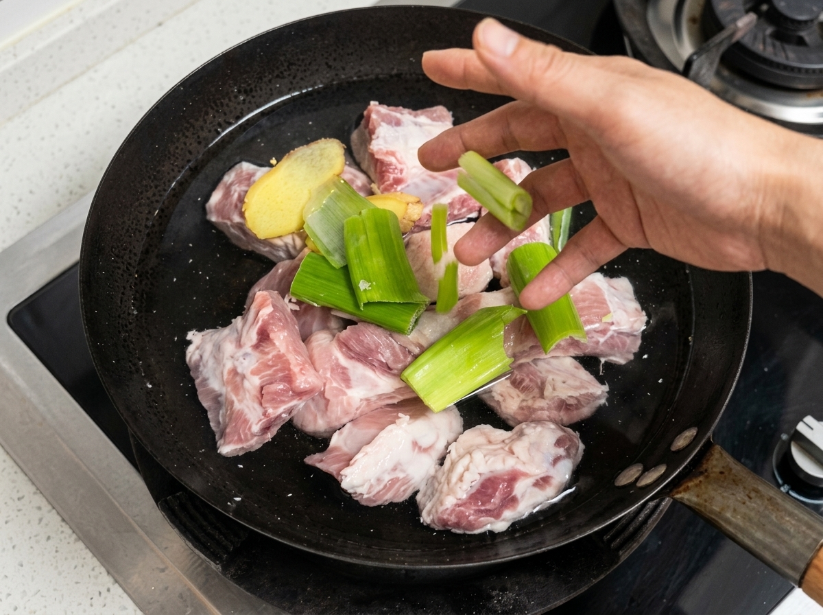 Costillas de cerdo, jengibre y cebolleta en una olla con agua fría listos para blanquear.
