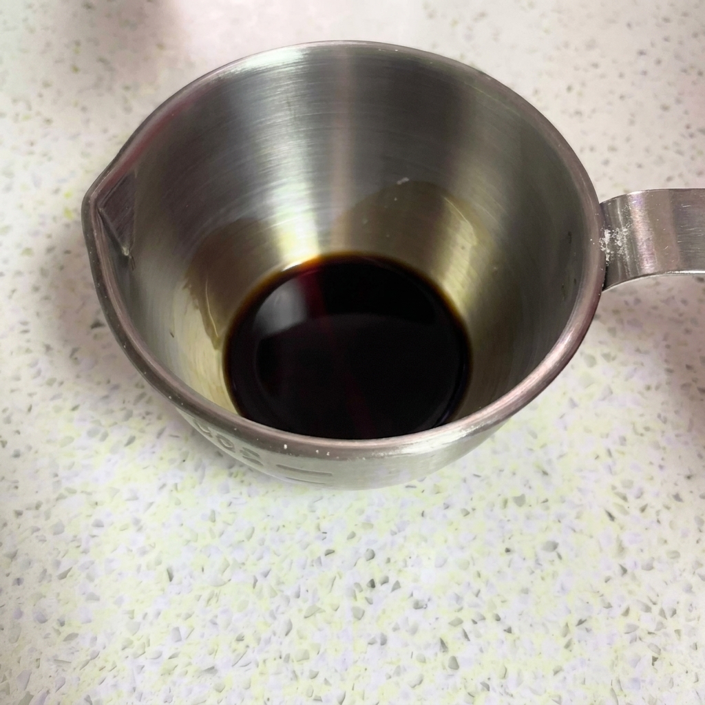 Salsa de soja oscura vertiéndose en una taza medidora de metal.