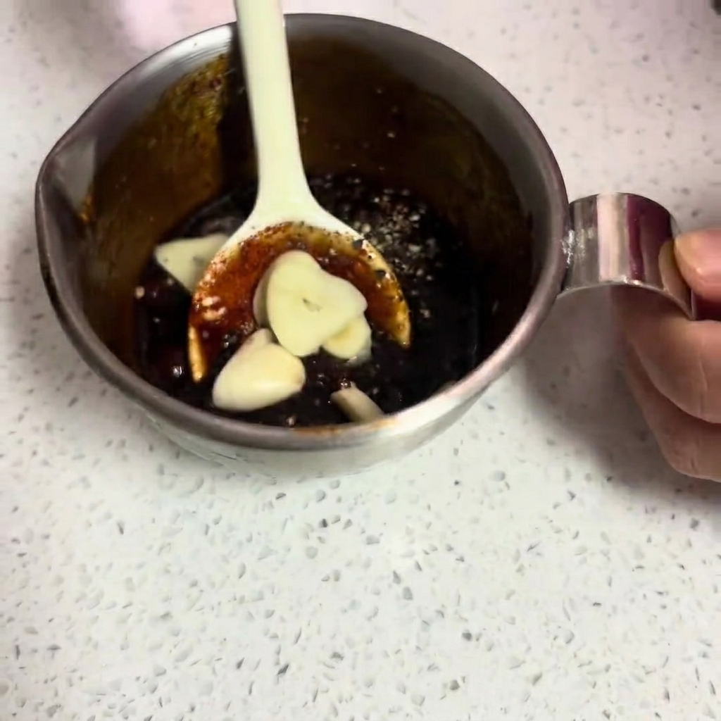 El marinado oscuro y espeso con láminas de ajo fresco siendo mezclado.