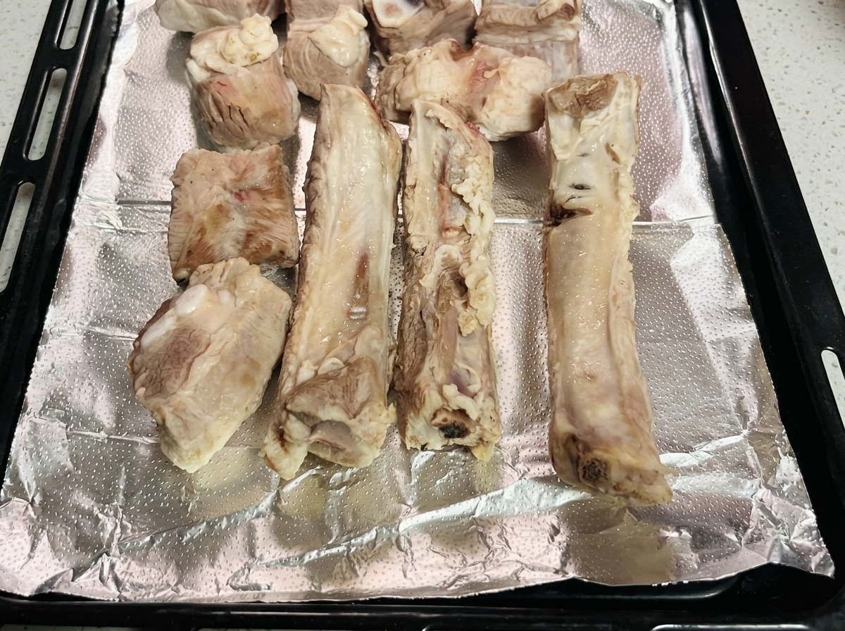Costillas de cerdo blanqueadas dispuestas ordenadamente sobre una bandeja con papel aluminio.