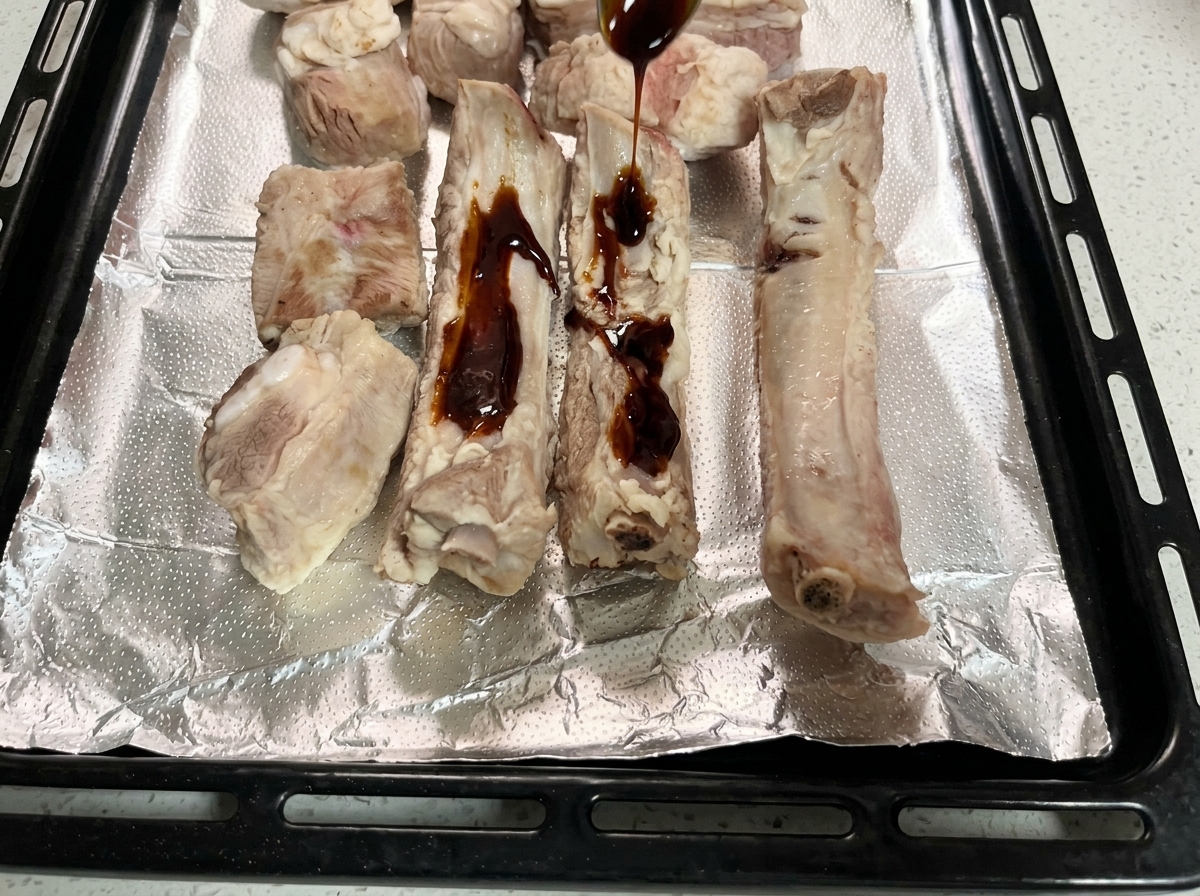 El marinado oscuro siendo vertido sobre las costillas crudas en la bandeja forrada.
