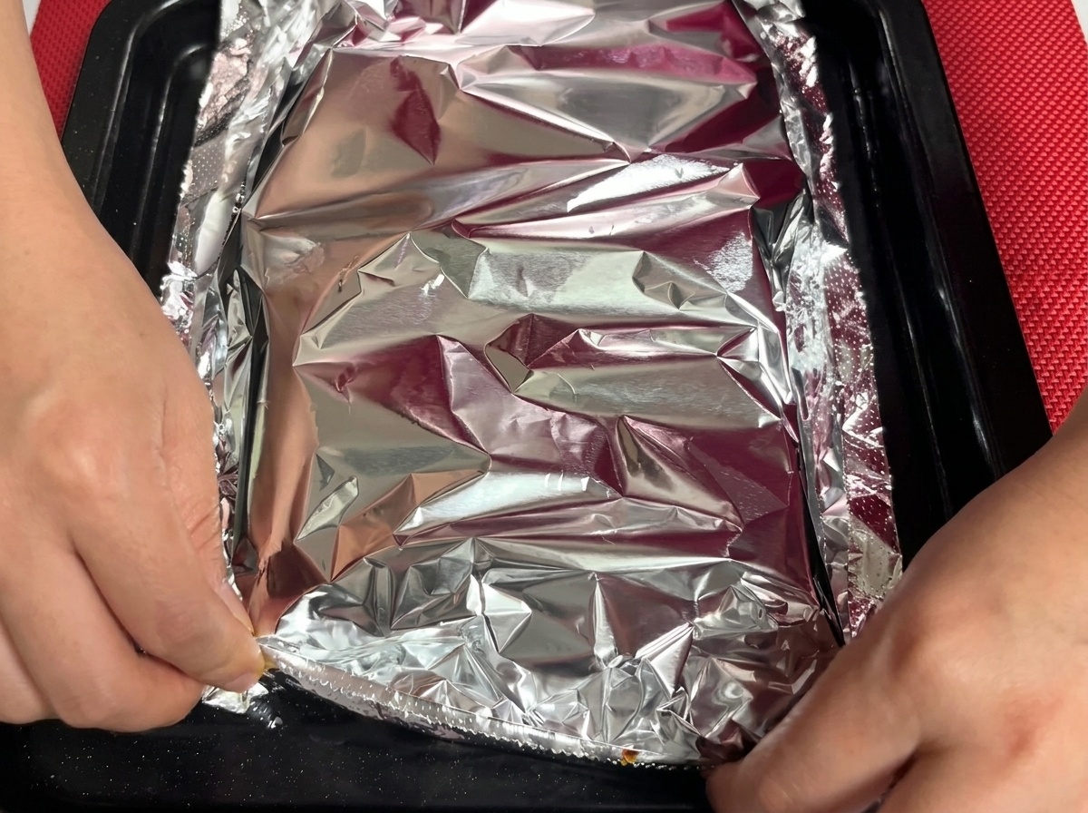 Una hoja de papel aluminio siendo sellada sobre la bandeja de costillas.