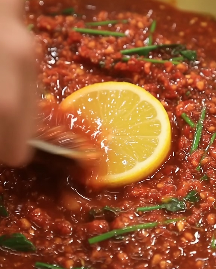 Aceite de sésamo dorado siendo vertido en el centro de la mezcla de adobo rojo.